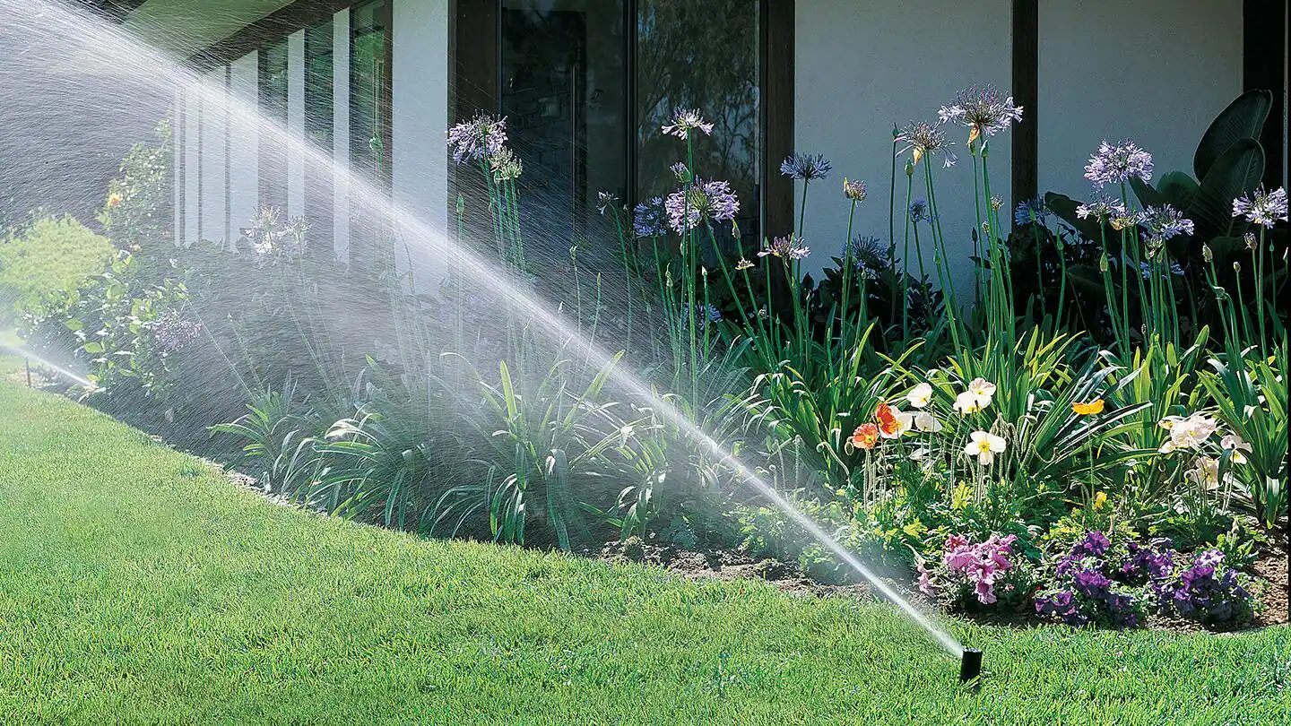 Sprinkler watering a flower bed beside a modern building
